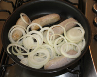 Sausages and onion rings in frying pan.